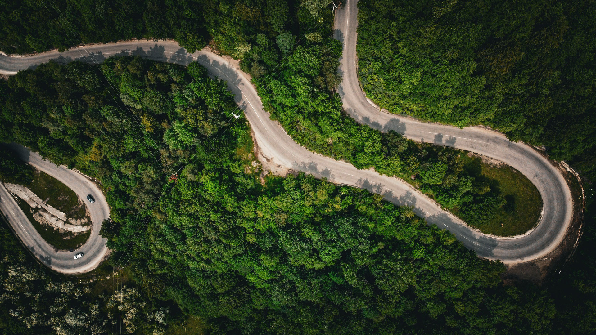 An aerial view of a winding road surrounded by lush green trees, showcasing sharp turns and a natural landscape.